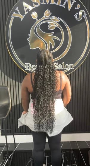 Long dark curly braids photographed from behind in front of the Yasmin's Beauty Salon sign